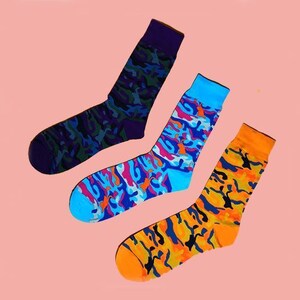 May include: Three pairs of colorful socks with a camouflage pattern. The socks are blue, orange, and purple with a white background.