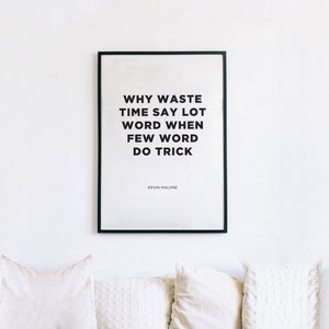 Puede incluir: Un estampado enmarcado con la cita "WHY WASTE TIME SAY LOT WORD WHEN FEW WORD DO TRICK" en texto negro sobre fondo blanco. La cita se atribuye a Kevin Malone. Debajo, tres cojines blancos.