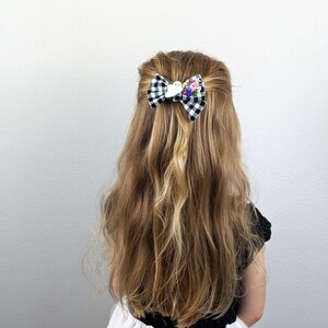 May include: A black and white checkered hair bow with a white bird and colorful flower embellishments.