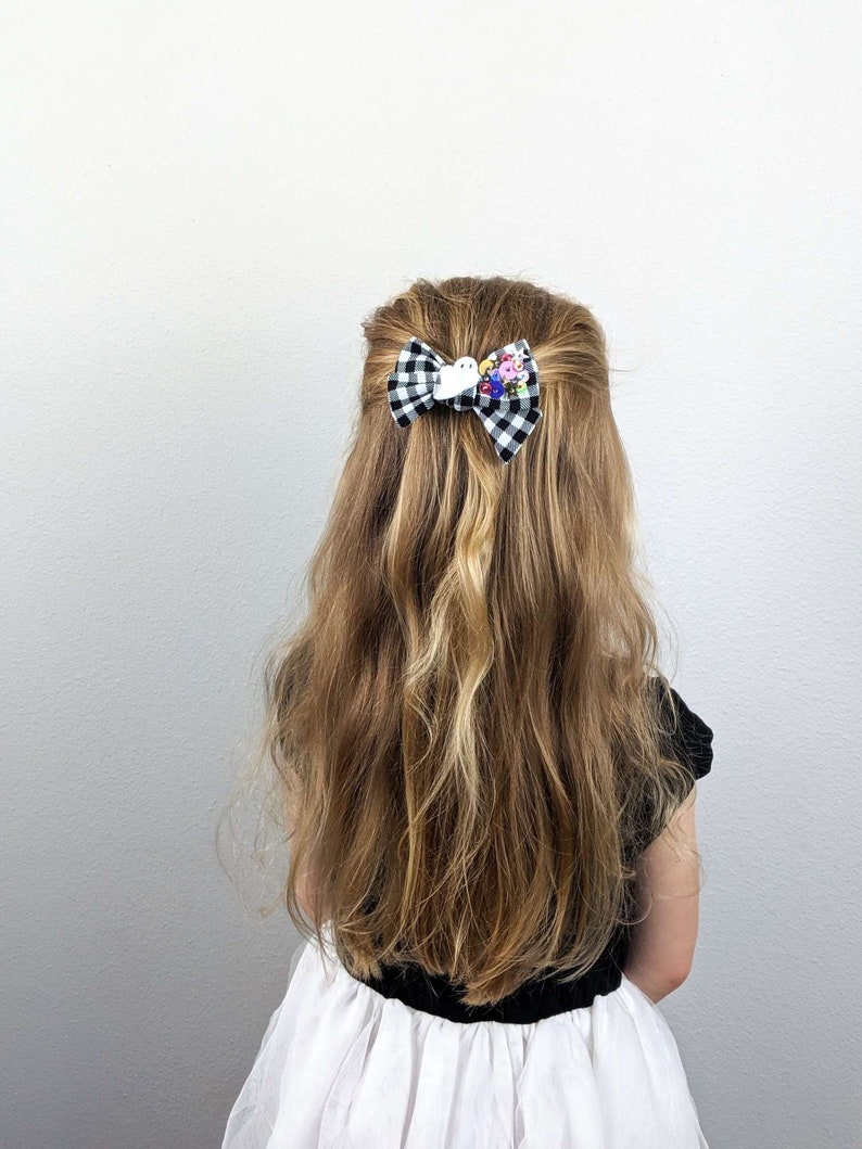 May include: A black and white checkered hair bow with a white bird and colorful flower embellishments.