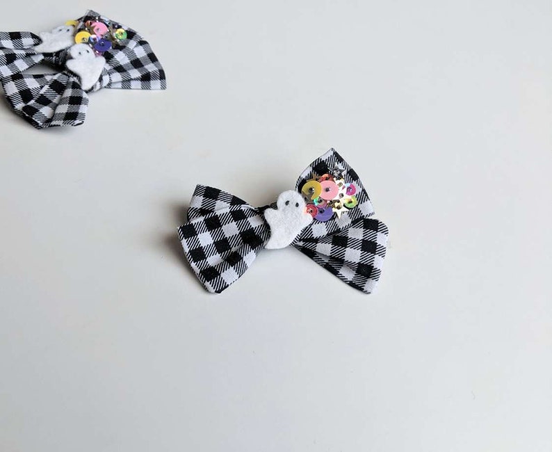 May include: Black and white checkered fabric bow with a white ghost and colorful sequins.