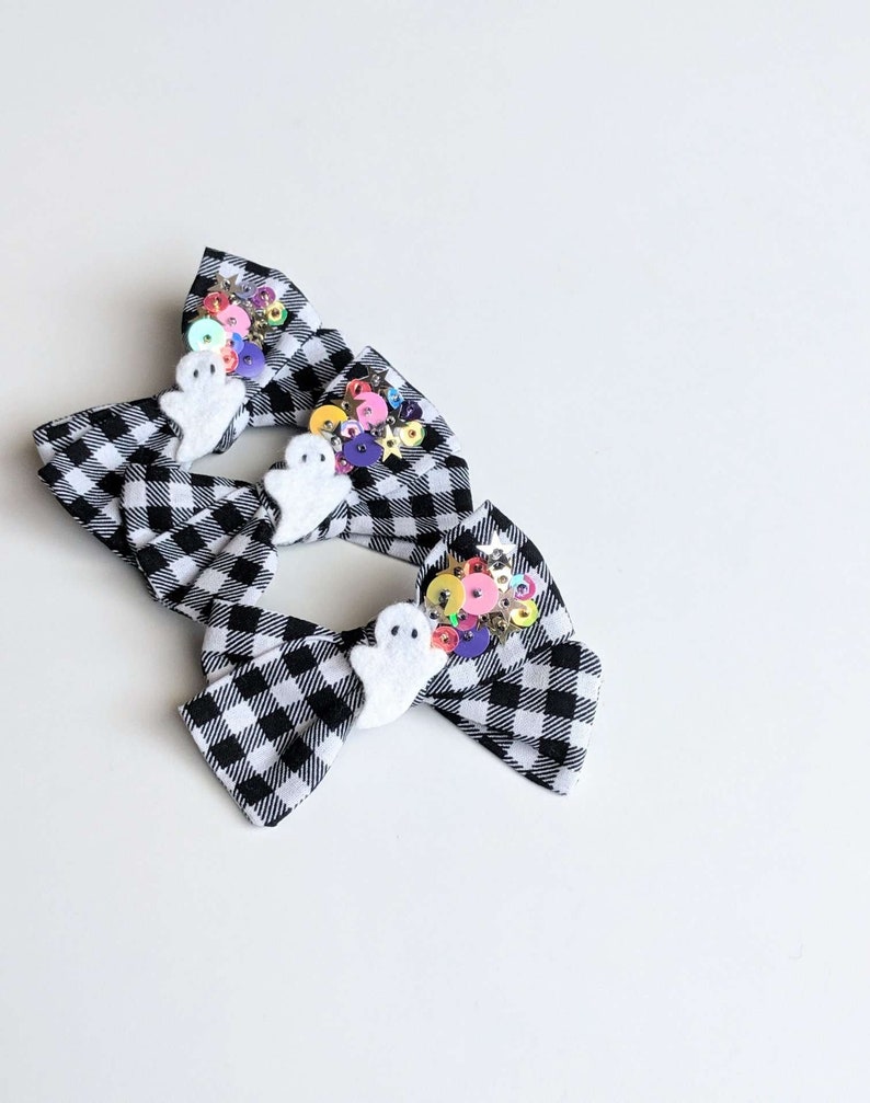 May include: Three black and white checkered hair bows with white ghost embellishments and colorful sequins.