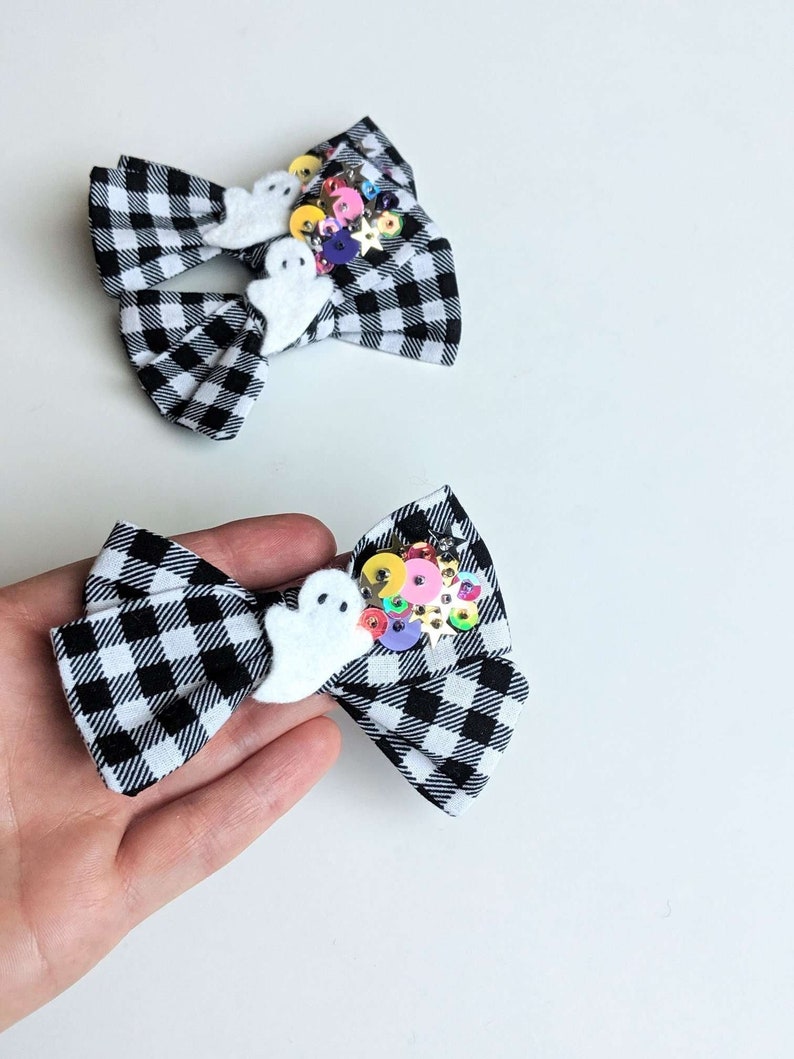 May include: Black and white checkered fabric bow with a white ghost and colorful sequins.