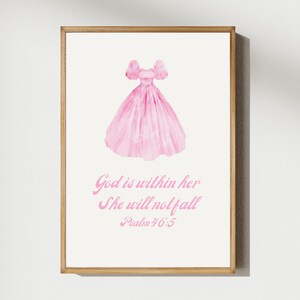 May include: A framed print featuring a watercolor illustration of a pink dress with puffed sleeves. Below the dress, the text reads "God is within her, She will not fall, Psalm 46:5" in pink script. The artwork is set against a cream background.