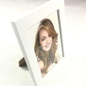 May include: White picture frame with a white mount and a photo of a woman with long brown hair. The frame is 6x8 inches and has a stand on the back.