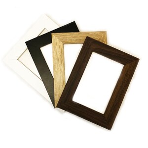 May include: Four picture frames in different colors: white, black, light brown, and dark brown. The frames are stacked on top of each other.