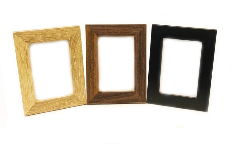 May include: Three picture frames in different colors: natural wood, dark wood, and black. The frames are all the same size and shape, and they are all empty.