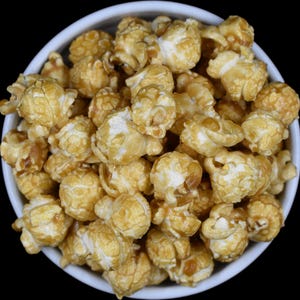 May include: A white bowl filled with caramel popcorn. The popcorn is golden brown and has a glossy finish.