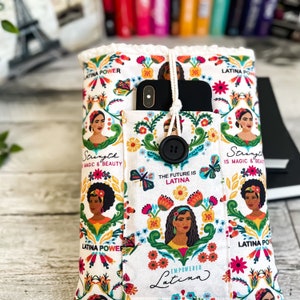 Könnte beinhalten: Eine weiße Stoff-Handyhülle mit einem bunten Blumenmuster und dem Text "Latina Power" und "The Future is Latina". Die Hülle hat einen Knopfverschluss und eine Tasche für ein Handy.