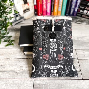 May include: Black and white phone case with a skeleton couple design. The case has a pocket for a phone and a button closure. The text "Till Death" is printed on the case.