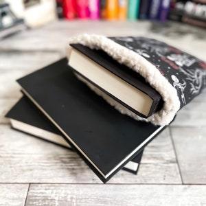 May include: A stack of three black hardback books with a white fluffy book cover on top. The book cover has a black and white design.