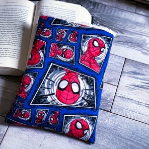 Puede incluir: Una cubierta de libro azul y roja con un patrón repetido de la cabeza de Spider-Man en un marco de estilo cómic. El fondo es azul con un patrón de remolino blanco y gris.