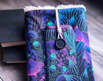 May include: A black fabric book cover with a white fuzzy lining. The cover features a colorful, abstract design with a pocket for a phone or other small item. A black button is attached to a white string.