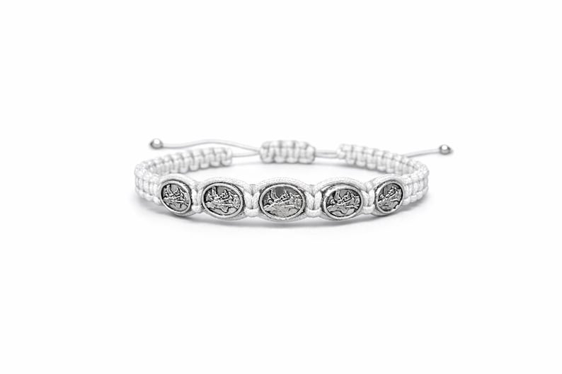 May include: White macram&eacute; bracelet with five silver-toned, circular charms. The charms are evenly spaced along the bracelet's centre. The bracelet has an adjustable sliding knot closure. The design is simple and elegant.