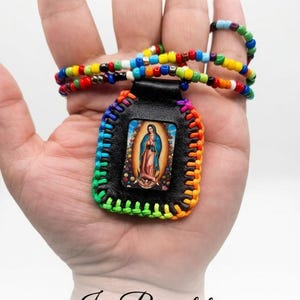 May include: A handmade necklace featuring a black leather pendant with a religious image, framed with rainbow stitching. The necklace has a beaded strap with colorful beads. The text "Jrs Bracelets" is visible.