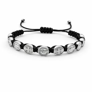 May include: Black braided cord bracelet featuring silver-toned circular charms. Each charm has a detailed design, with a cross and other symbols. The bracelet is adjustable with a sliding knot closure, suitable for various wrist sizes.