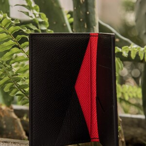 May include: A black leather wallet with a red interior. The wallet is closed and has a textured surface.