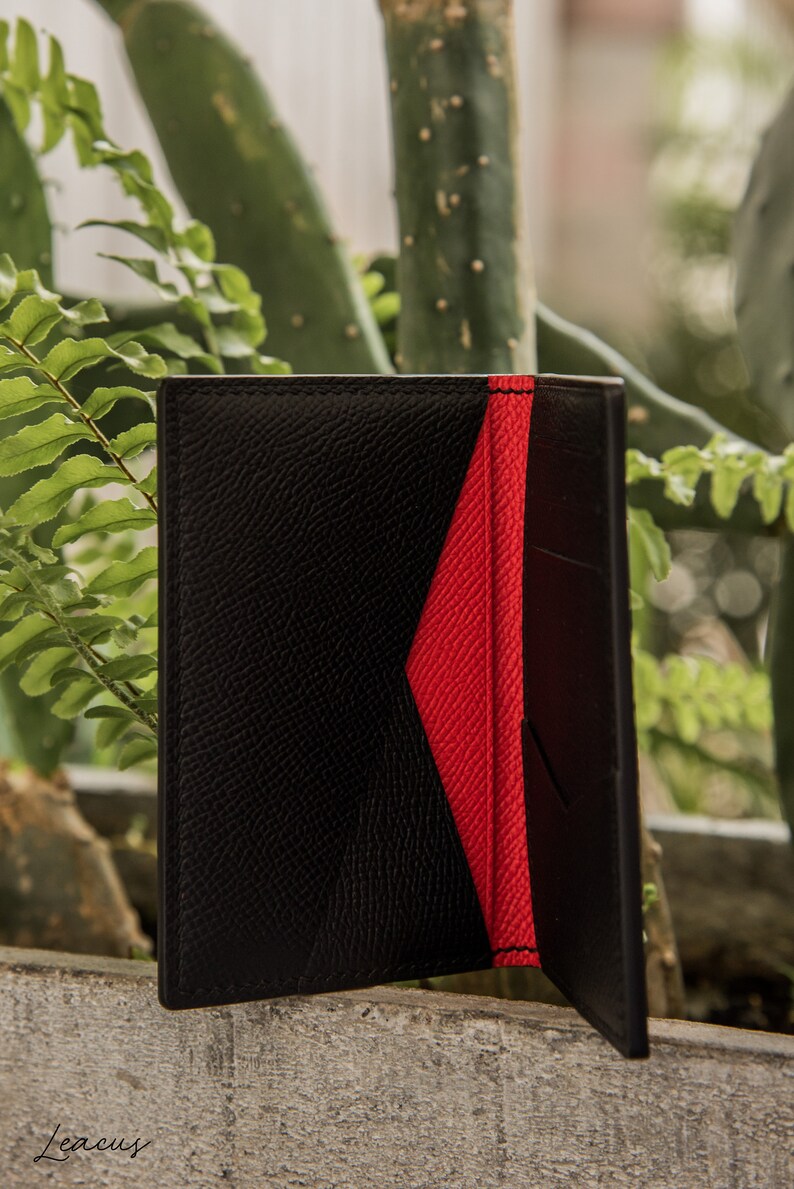 May include: A black leather wallet with a red interior. The wallet is closed and has a textured surface.