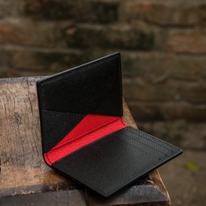 May include: A black leather wallet with a red interior. The wallet is folded open and is sitting on a wooden surface.