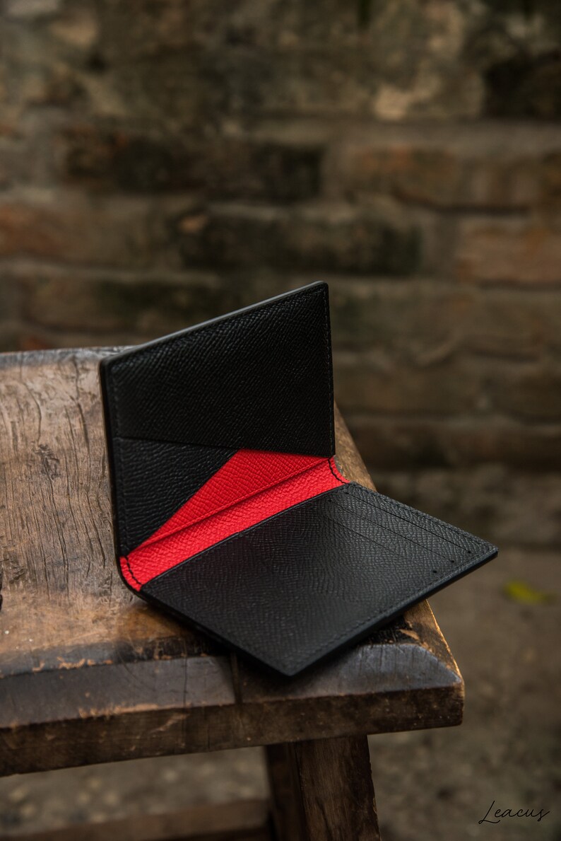 May include: A black leather wallet with a red interior. The wallet is folded open and is sitting on a wooden surface.