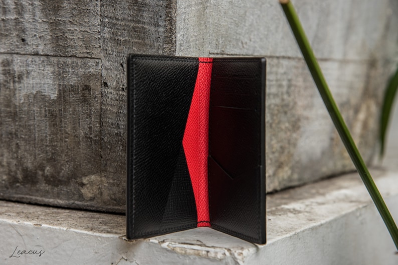 May include: A black leather wallet with a red interior. The wallet is open and the inside is visible. The wallet is on a gray surface.