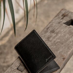 May include: A black leather wallet with a subtle textured finish. The wallet is folded in half and has a small embossed logo on the front.