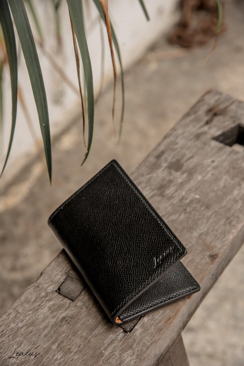 May include: A black leather wallet with a subtle textured finish. The wallet is folded in half and has a small embossed logo on the front.
