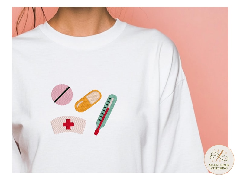 May include: A white long-sleeve shirt featuring an embroidered design of a pink round pill with a black line, an orange capsule, a teal thermometer with a red tip, and a white nurse cap with a red cross symbol centered on the front chest area.