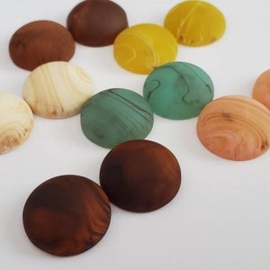 May include: Assortment of round, colorful, decorative cabochons with marbled patterns. The cabochons are in shades of brown, beige, green, and yellow.