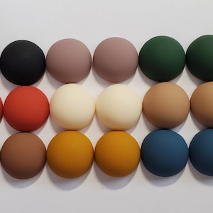 May include: A collection of 18 round, flat, matte polymer clay cabochons in various colors, including black, brown, red, green, beige, and blue.