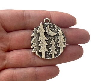 May include: Silver charm with a textured circular design featuring a crescent moon and four stylised pine trees.
