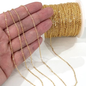 May include: A spool of gold-colored chain, with a few strands of the chain laid out on a hand. The chain is a delicate, fine-link style.