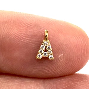 Puede incluir: Encanto de oro con la letra A, incrustado con pequeñas piedras de circonita cúbica transparentes.