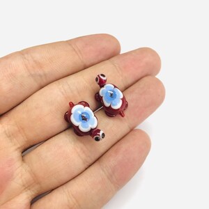 May include: Two small glass turtle figurines with red bodies, white and blue flower designs on their shells, and black eyes.