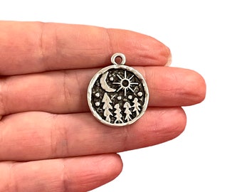 May include: Silver charm featuring a moon, sun, and pine tree design. The charm is round and has a textured surface.