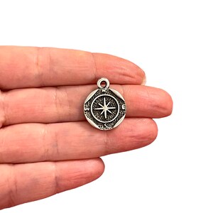 May include: Silver compass charm with a star in the center and the letters N, S, E, and W around the edge.
