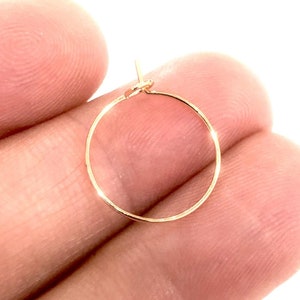 May include: A gold hoop earring with a simple, circular design. The earring is shown being held by a hand.