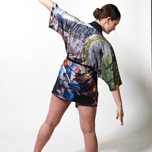 May include: A colorful kimono-style robe with a black belt. The robe features a print with a mix of colors and a landscape design. The model is wearing the robe and is in a dance pose. The robe is made of a soft, flowing fabric.