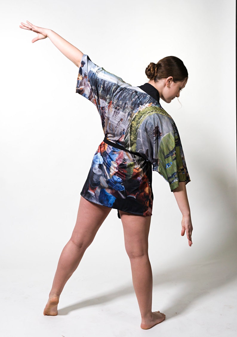 May include: A colorful kimono-style robe with a black belt. The robe features a print with a mix of colors and a landscape design. The model is wearing the robe and is in a dance pose. The robe is made of a soft, flowing fabric.