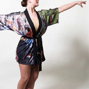 May include: A colorful kimono-style robe with a black trim and belt. The robe features a vibrant print of an Impressionist painting, with figures and landscapes. The sleeves are wide, and the robe is knee-length.
