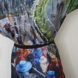 May include: A kimono-style garment featuring a vibrant, impressionistic painting of a horse race scene. The artwork depicts spectators in hats and suits, with a racetrack and horses visible. The garment is cinched at the waist with a black belt.