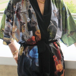 May include: A colorful kimono-style robe with a black trim and belt. The robe features a print of a painting with figures in hats and coats, set against a green and blue background. The robe is made of a lightweight fabric.