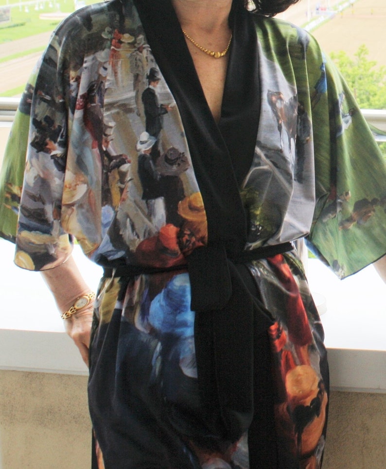 May include: A colorful kimono-style robe with a black trim and belt. The robe features a print of a painting with figures in hats and coats, set against a green and blue background. The robe is made of a lightweight fabric.