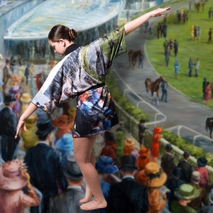 May include: A short kimono-style robe with a colorful print featuring a horse race scene. The robe is black with a white collar and sleeves. The background is a painting of a horse race with spectators.