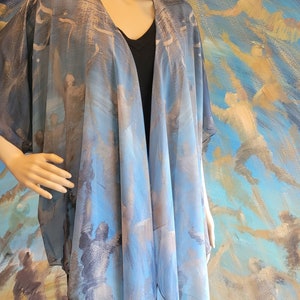 May include: A sheer, open-front kimono in shades of blue, gray, and beige. The fabric features an abstract print with figures and brushstrokes. The kimono is draped over a black top and is displayed on a mannequin.