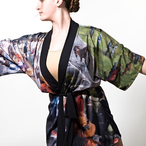 May include: A colorful kimono-style robe with a black trim and belt. The robe features a vibrant print of a horse race scene. The robe is worn over a beige top.