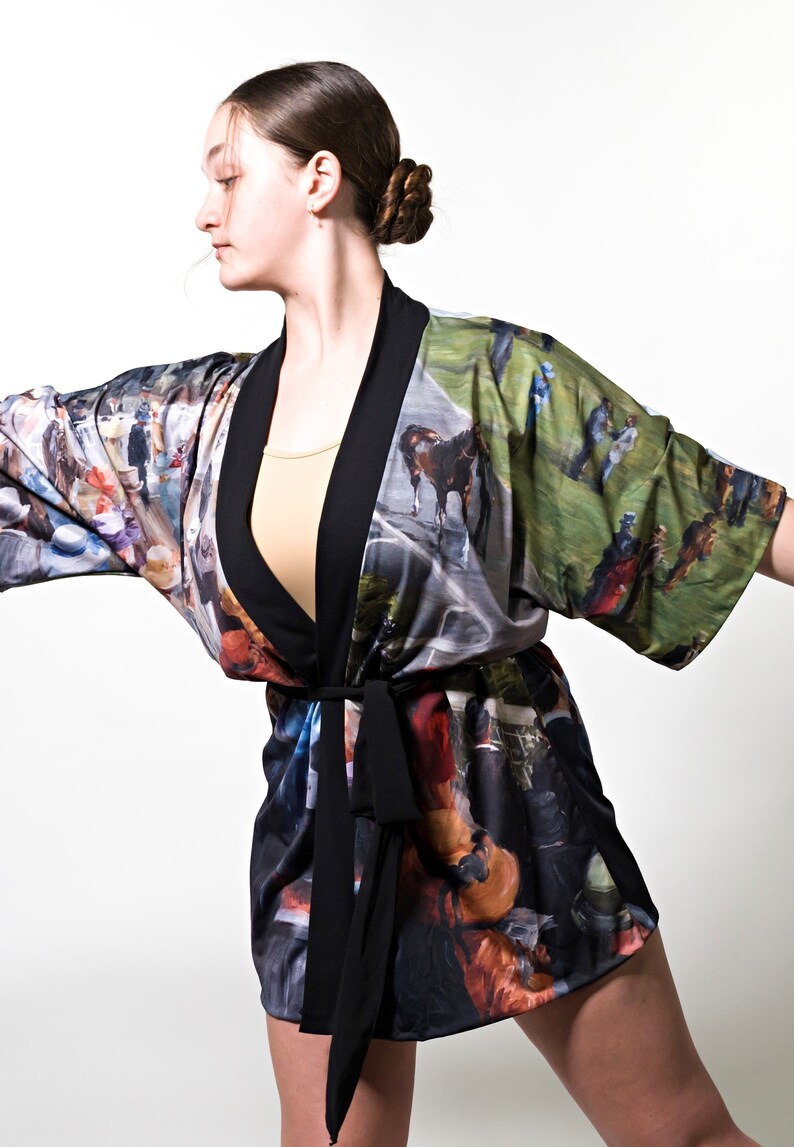 May include: A colorful kimono-style robe with a black trim and belt. The robe features a vibrant print of a horse race scene. The robe is worn over a beige top.