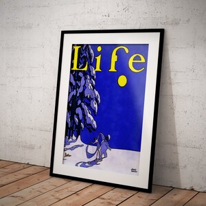 May include: Framed vintage "Life" magazine cover art. The artwork features a winter scene with figures skiing, a snow-covered tree, and the word "Life" in yellow. The background is a deep blue, and the frame is black.