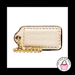 May include: A white leather Coach key chain with a gold chain and a brown leather tag. The tag has the word "Coach" embossed on it.