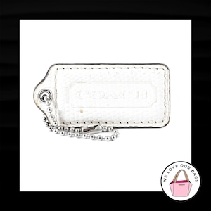 May include: White leather Coach key chain with a silver chain and a silver loop. The key chain has the word "COACH" embossed on it.